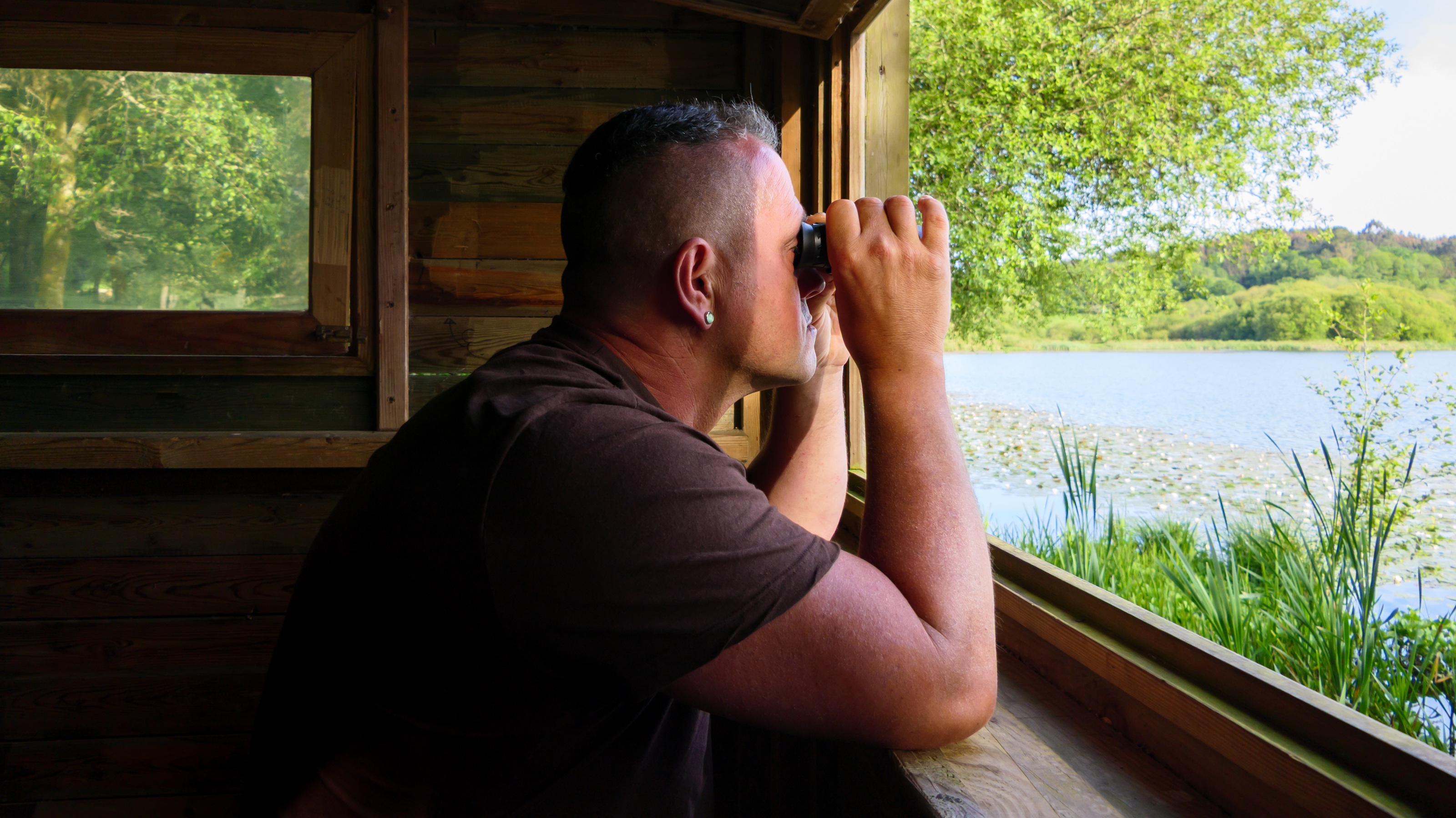 A man inside a cabin uses binoculars to look outside. 