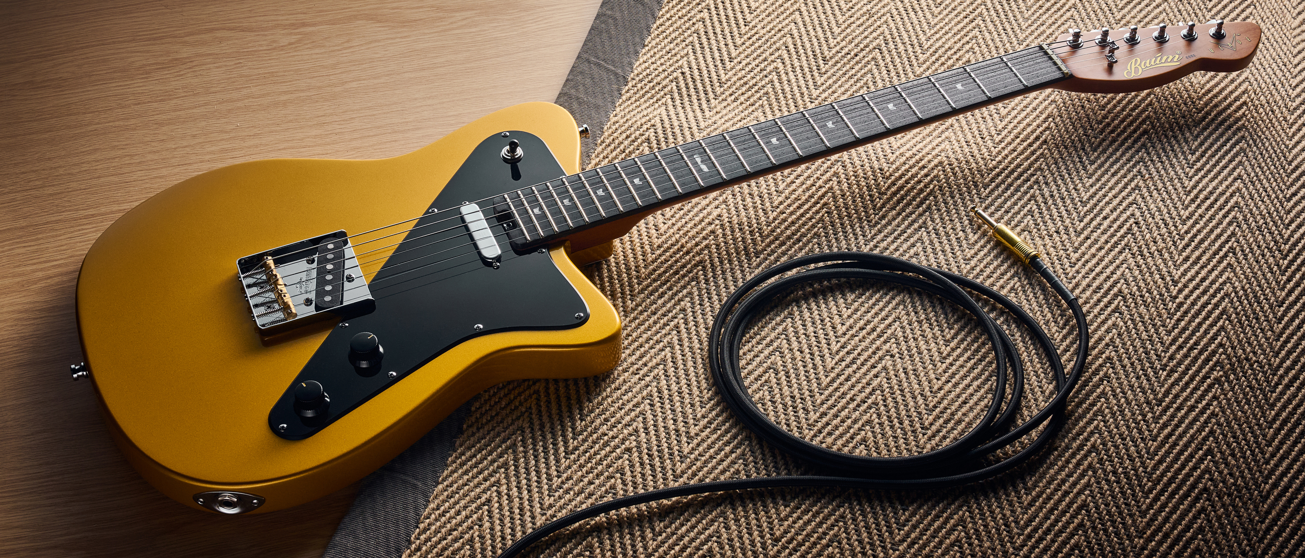 A Baum Guitars Verve electric guitar lying on a rug with a guitar cable coiled nearby