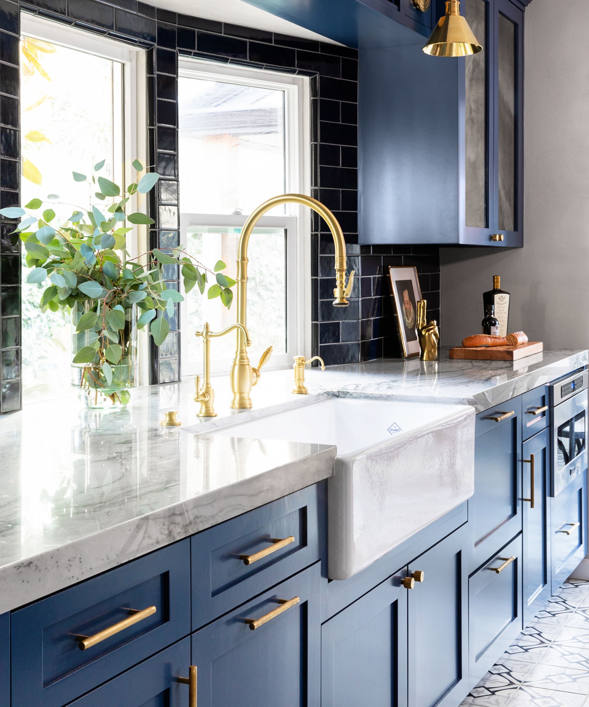 A small kitchen with dark blue cabinets, marble countertops, brass taps and fixtures.