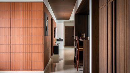 Hallway looking through into kitchen with vertical terracotta tile walls, dark wood panelling and dark wood bar stools