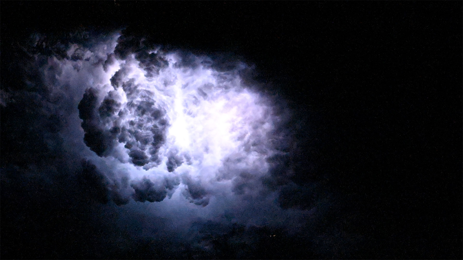 a bright white flash of light from lightning lights up a cloud as seen at night from above Earth