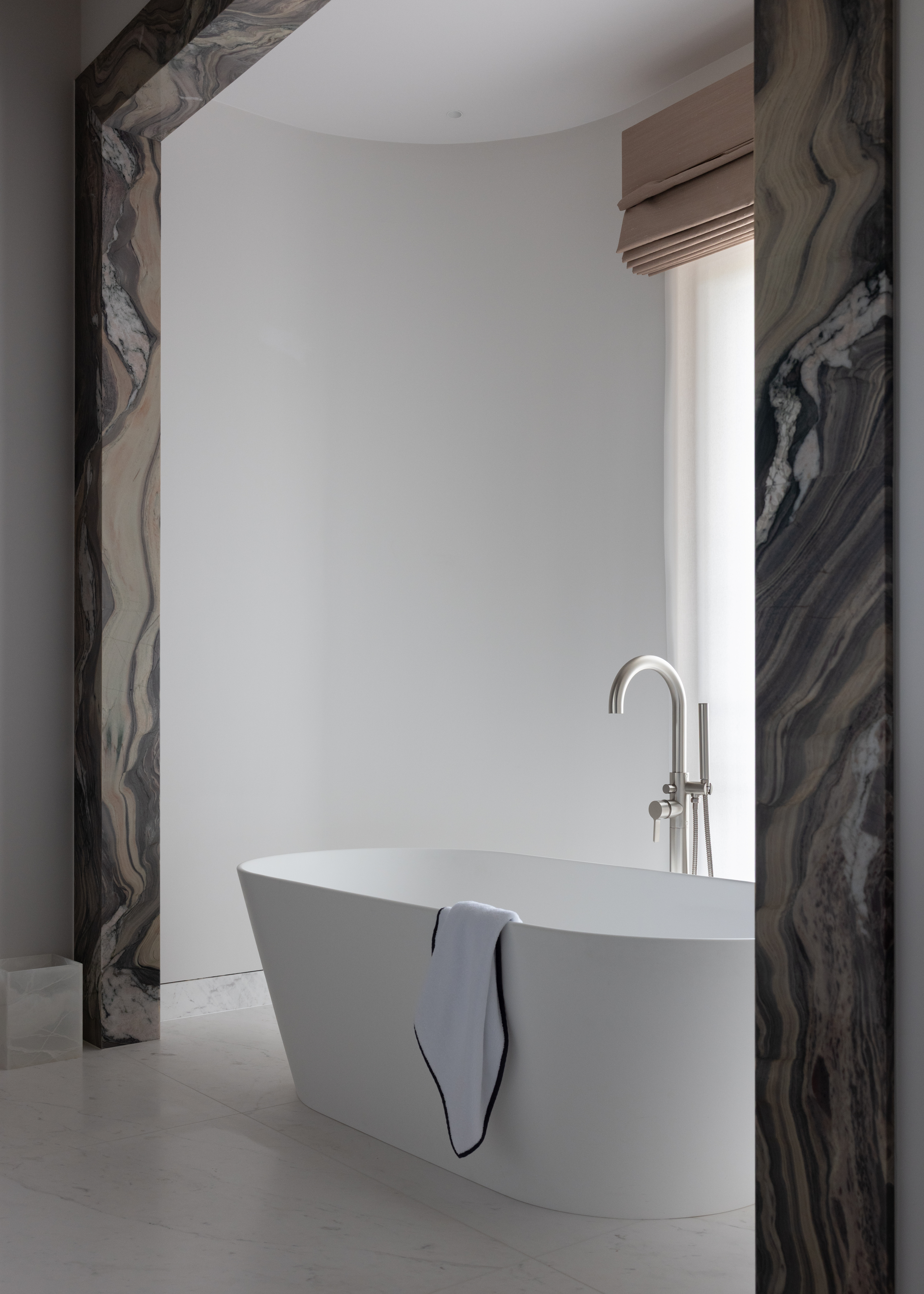 a dark marble architrave framing an all white bath area with a freestanding tub