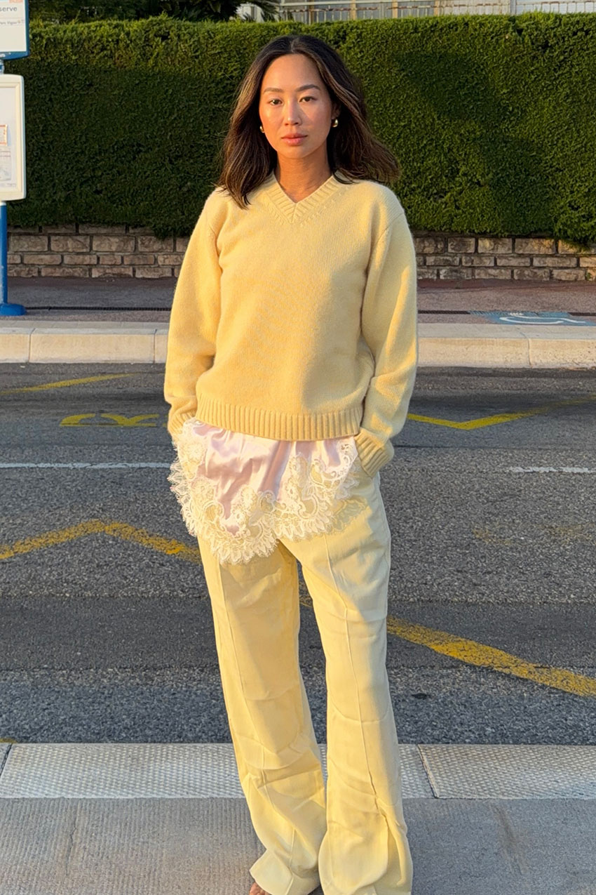 a woman wearing a butter yellow sweater, lace-trim top, and butter yellow pants