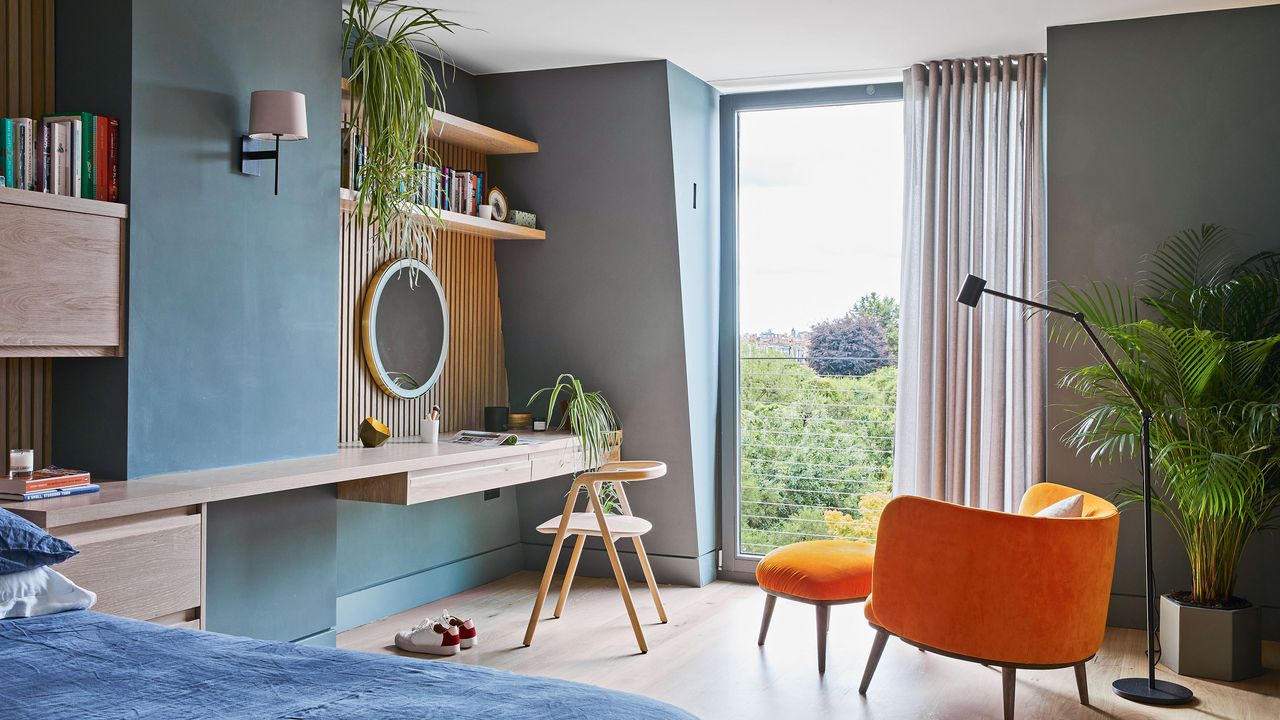 Blue bedroom with dressing table and large floor to ceiling window with orange accent chair infront