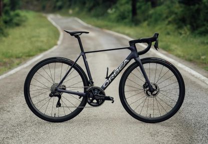 The Orbea Orca OMX on a tarmac road with greenery either side 