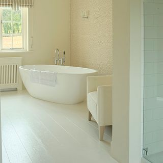 bathroom with white bath tub armchiar and delicate small print wallpaper