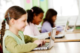 Three smiling girls using laptops in the classroom