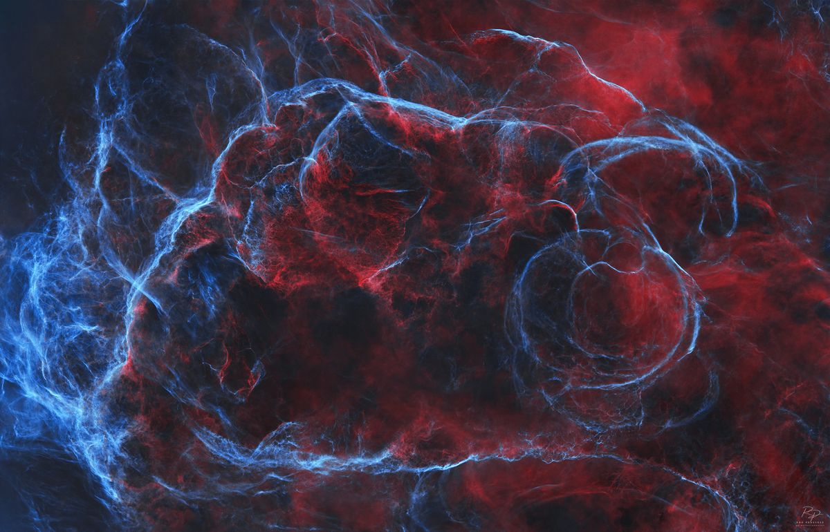 A deep space nebula scene is shown, featuring swirling masses of colorful interstellar gas and dense, dark dust filaments.