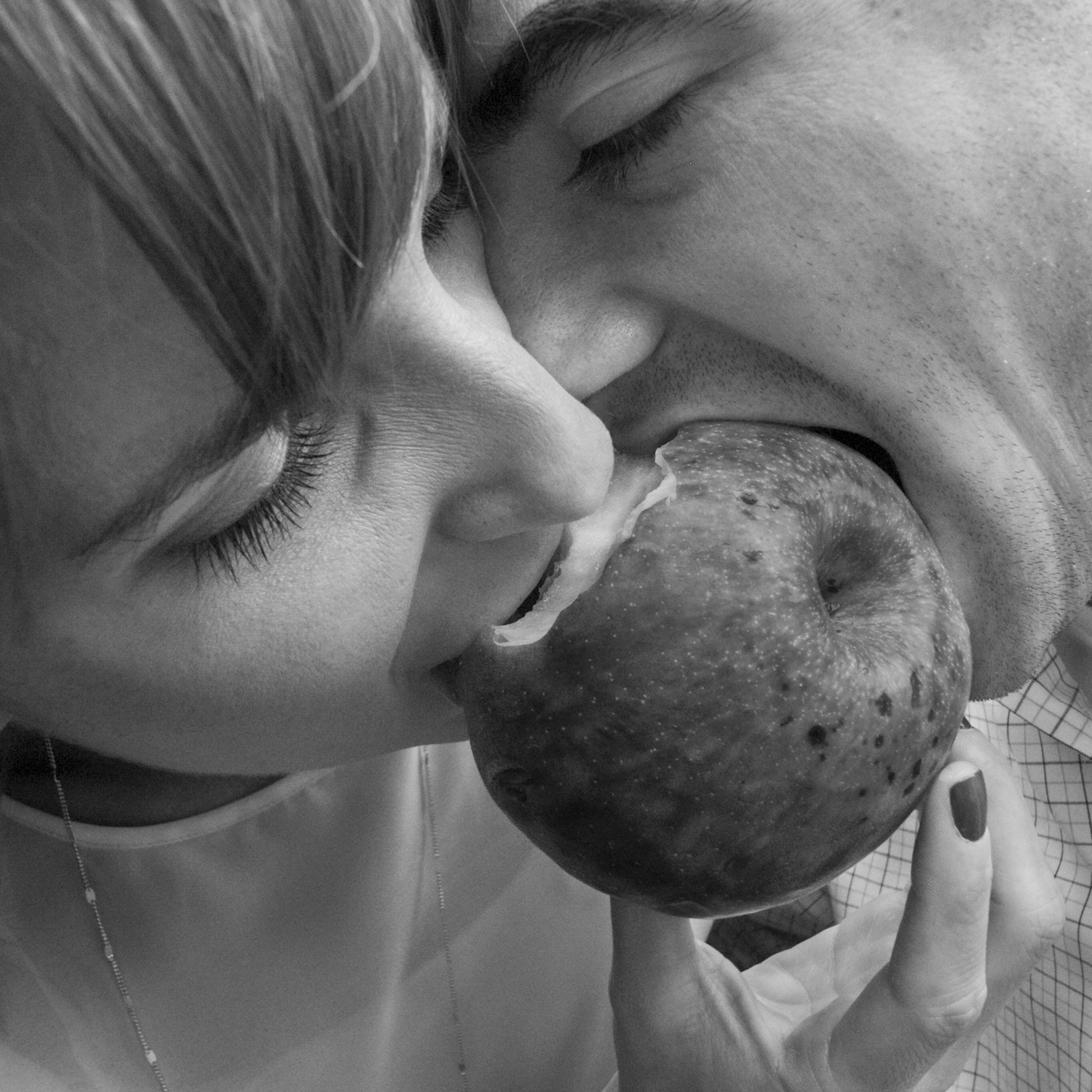 Black and white photo of two people biting into the same apple