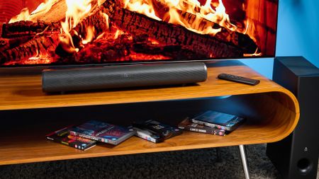 the creative stage pro soundbar and subwoofer, a super-budget home cinema system with 2.1 channels and a remote control photographed on a wooden tv stand with a TV behind