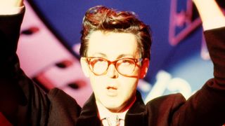 Paul McCartney performing on stage, dressed as Buddy Holly