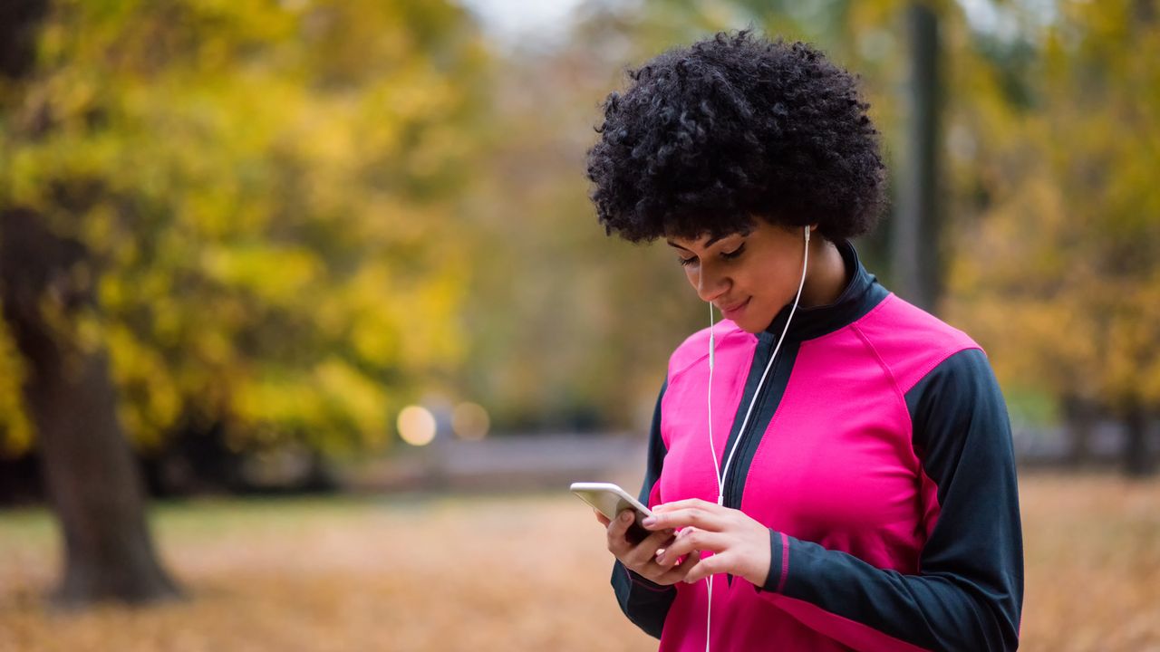 Women wears headphones and is on her phone before she begins a run outside