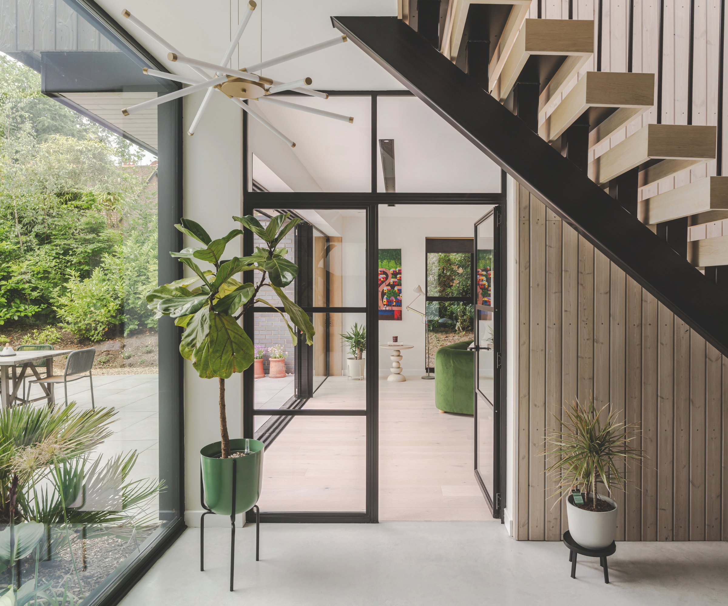 On the left, a glass wall window overlooking patio. Straight ahead, a black panelled doorway leading into the living area. Up above to the right, the staircase partly in shot