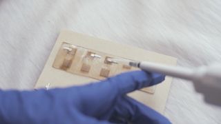 A person holds a pipette on a rectangular piece of material