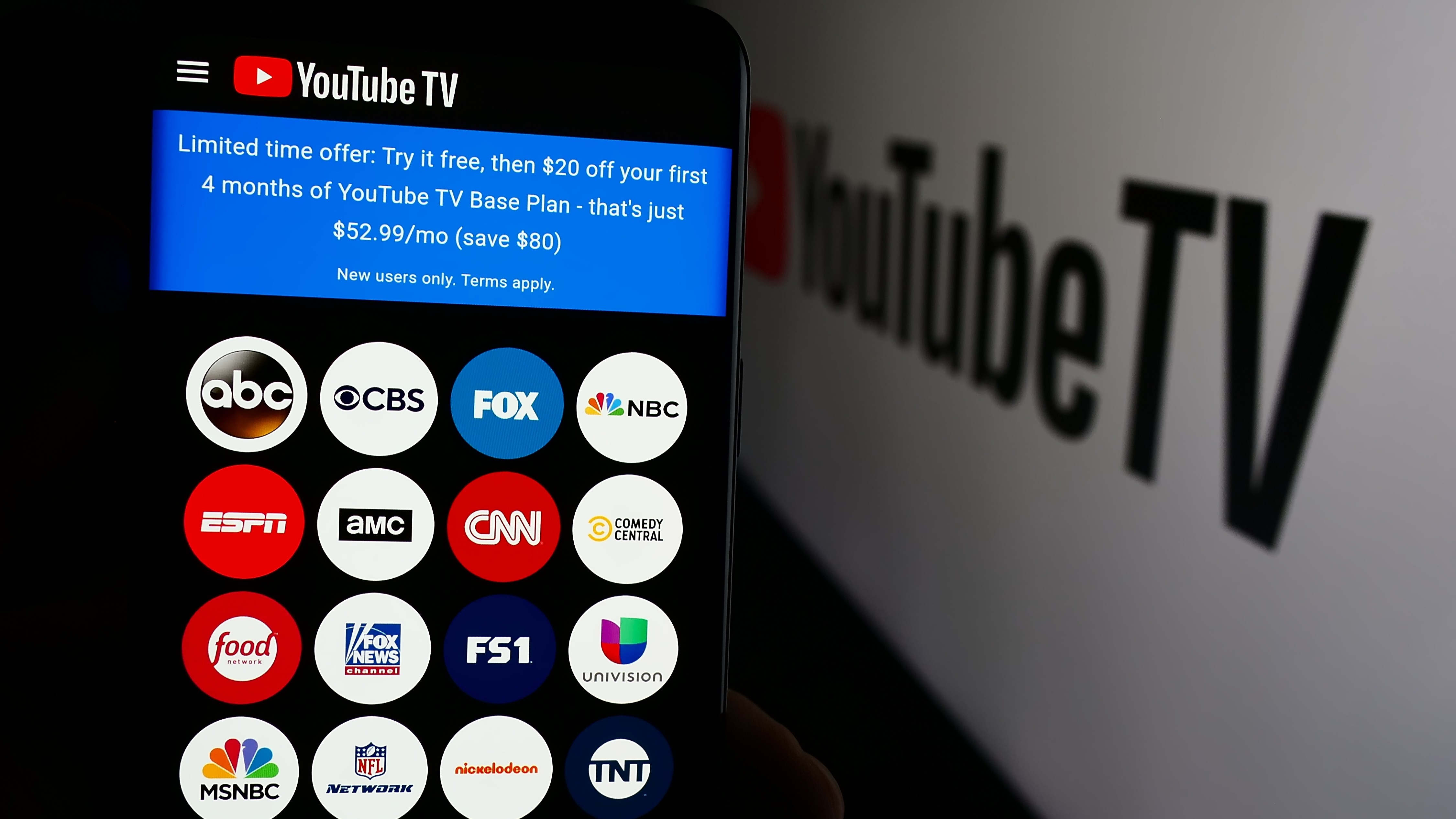 Person holding cellphone with webpage of YouTube TV in front of business logo.