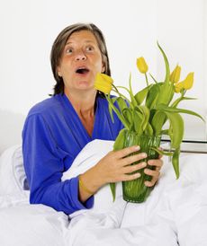 Woman In Bed Holding A Vase Of Flowers