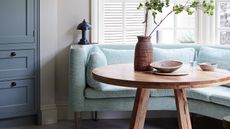 kitchen diner with aqua sofa, aqua patterned cushions, round wooden table and white shutters