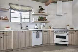 kitchen with white walls and pale wood cabinets with oven set in corner of room grey blind and open shelves