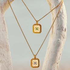 2 gold Missoma necklaces with square pendants hanging from white wood