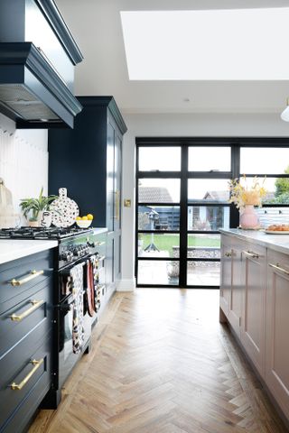 Shaker-style kitchen with blue base cabinets and pink kitchen island, with aluminium Crittall-style doors leading to the garden