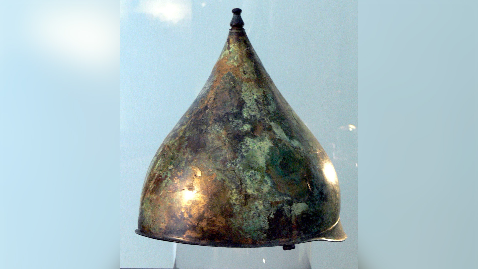 A conical metal helmet with a green patina