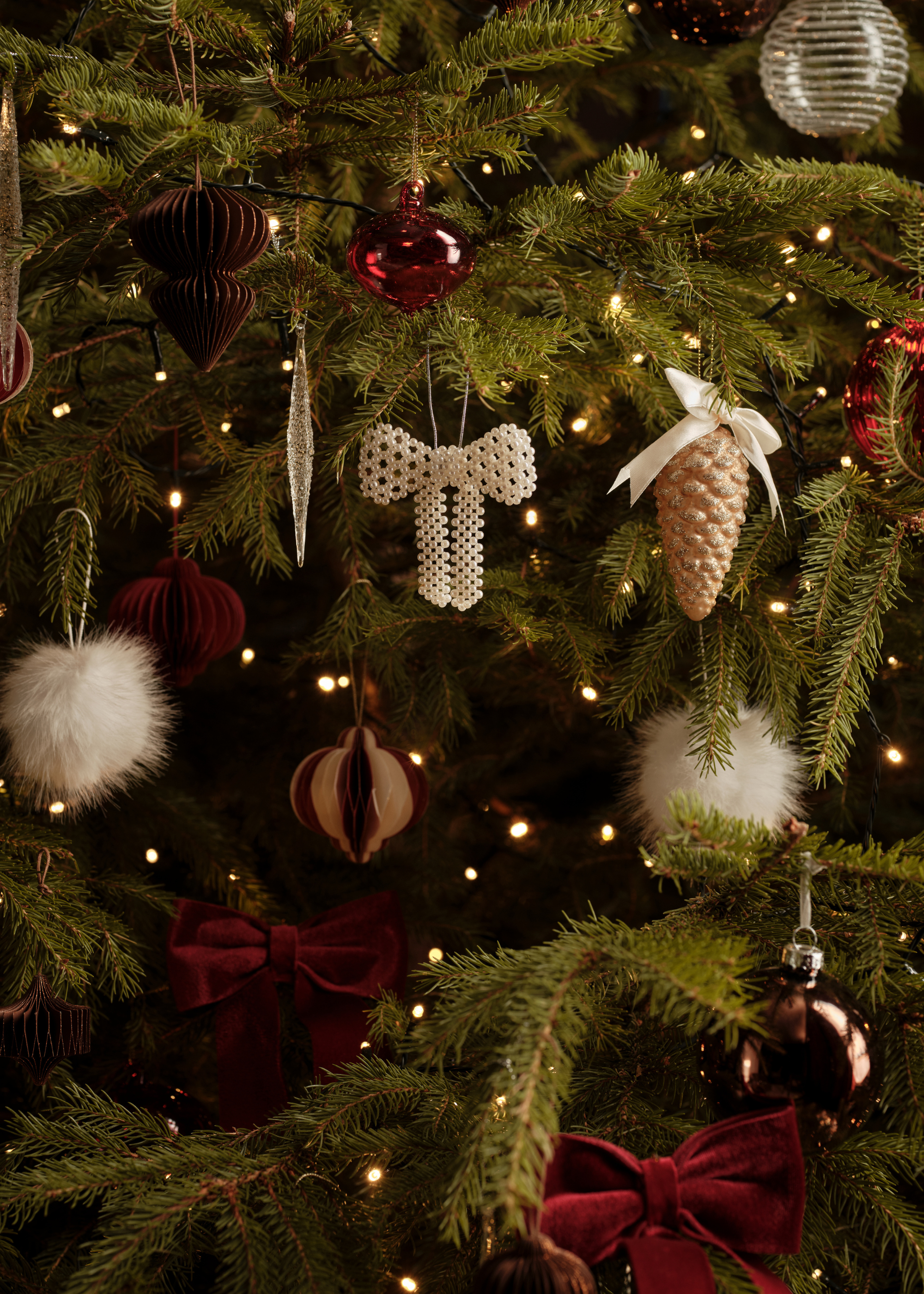 A close-up of a tree with fluffy baubles, glass baubles, pearl bows, and velvet bows