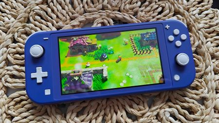 Nintendo Switch Lite in Blue sitting on wicker table with Zelda: Link's Awakening on screen.