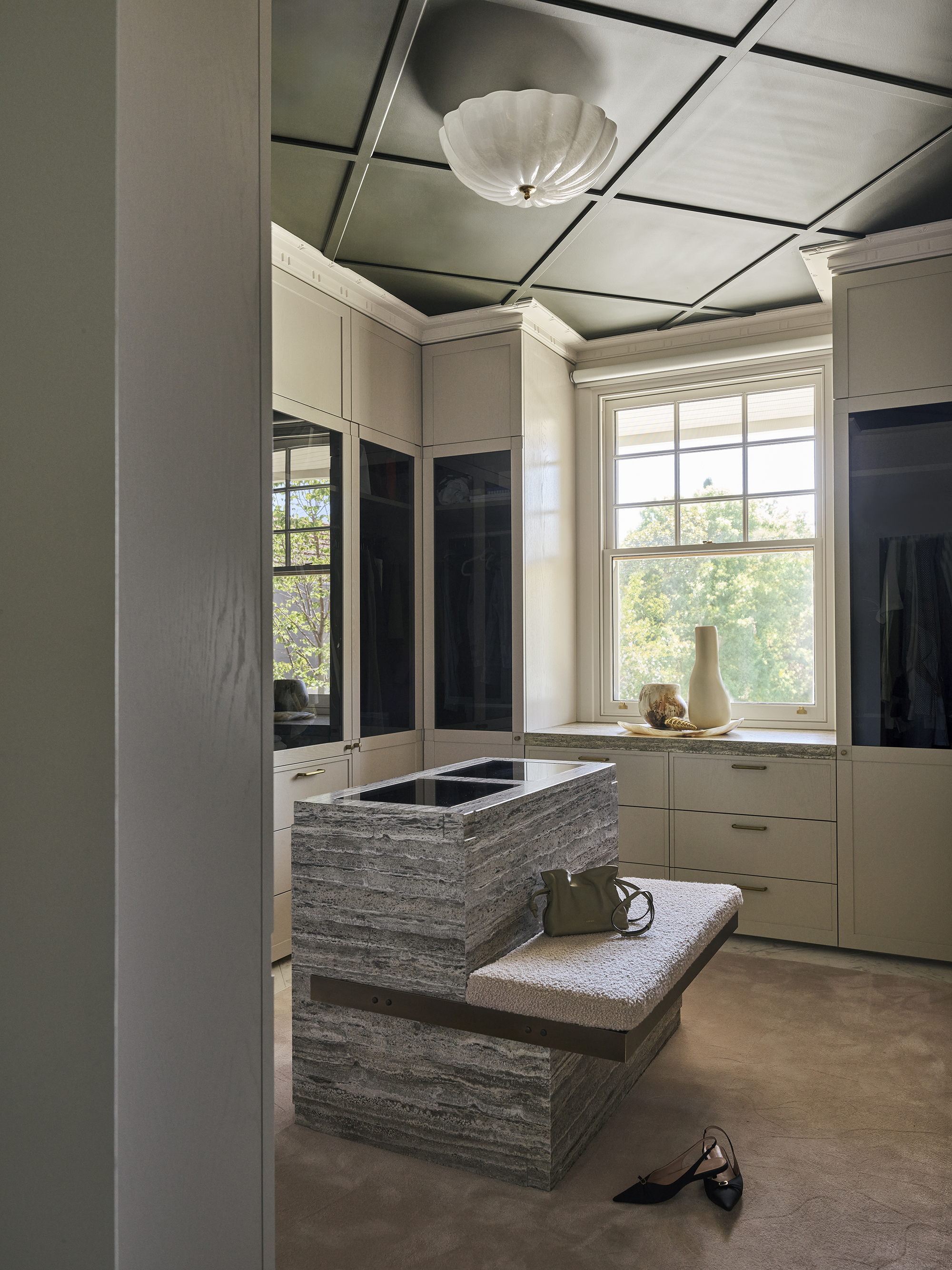 walk in wardrobe with marble closet island with built-in seat, with cabinets, decorative ceiling detail, and mirrored doors