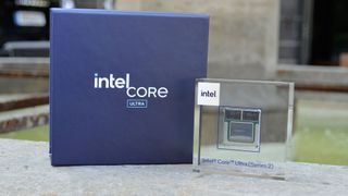 An Intel Lunar Lake chip in a plastic case next to an Intel Core Ultra Box in front of a fountain