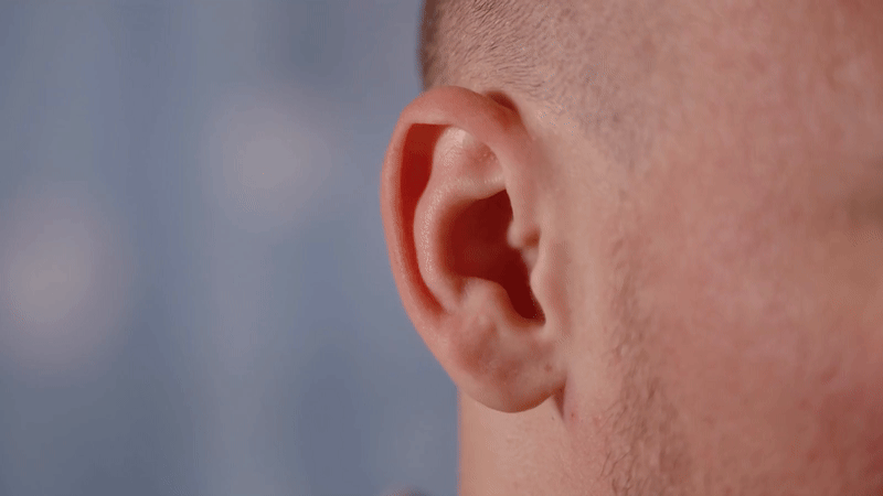 Expressive bald man with healthy skin shows ability to wiggle ears having fun on light blue background in room extreme closeup