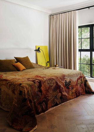 A stylish bedroom with a vintage bedspread, a side table and large windows