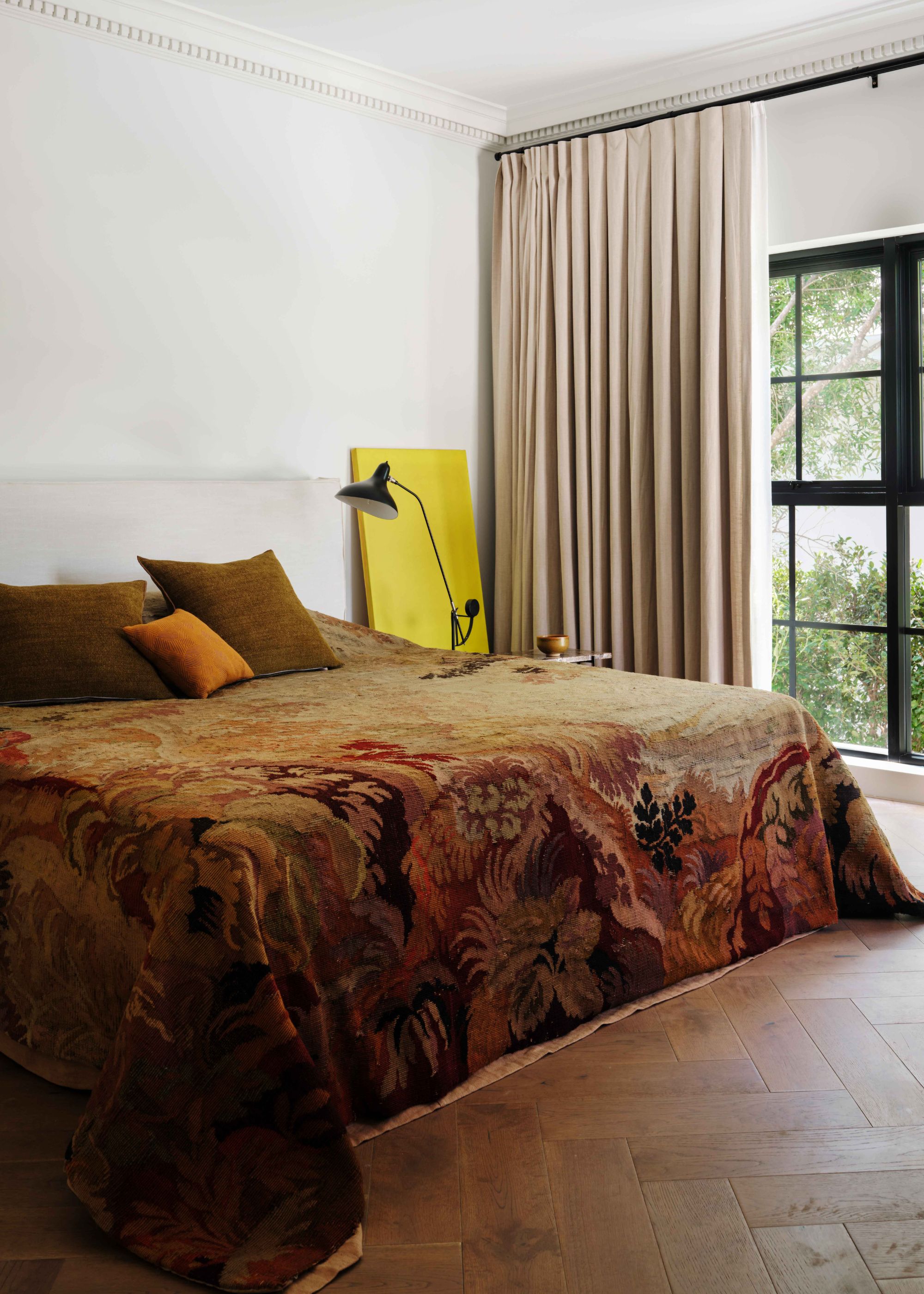 A stylish bedroom with a vintage bedspread, a side table and large windows