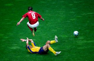 Denmark's Jon Dahl Tomasson jumps over Sweden's Erik Edman during their 2-2 draw in the 2004 European Championships. | Location: Porto, Portugal.