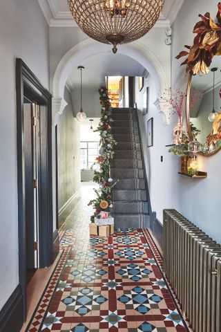 Lucy Kemp's red and blue patterned floor tiles in entryway with printed dark runner and blue painted door frame