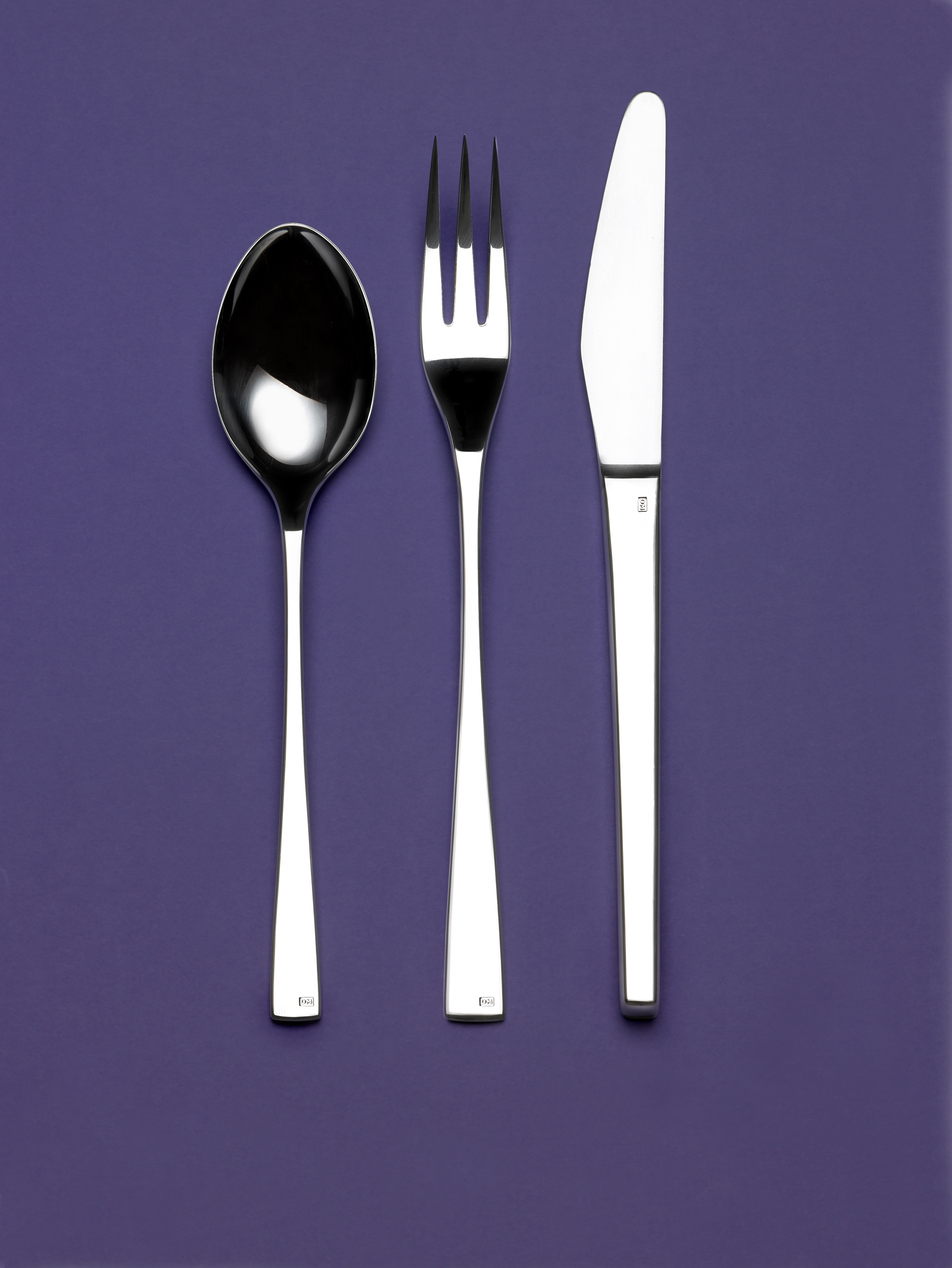A silver spoon, fork and knife on a purple background