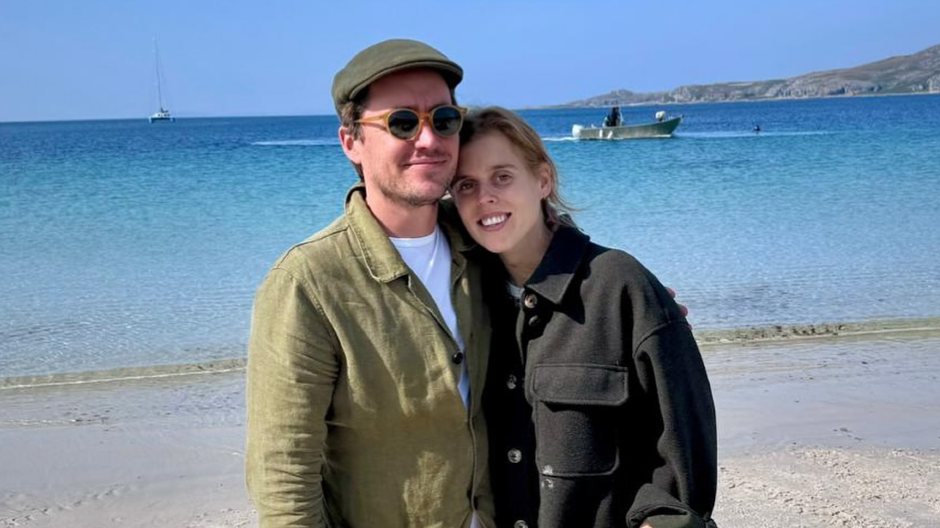 Princess Beatrice and Edoardo Mapelli Mozzi wearing green jackets on the beach and smiling
