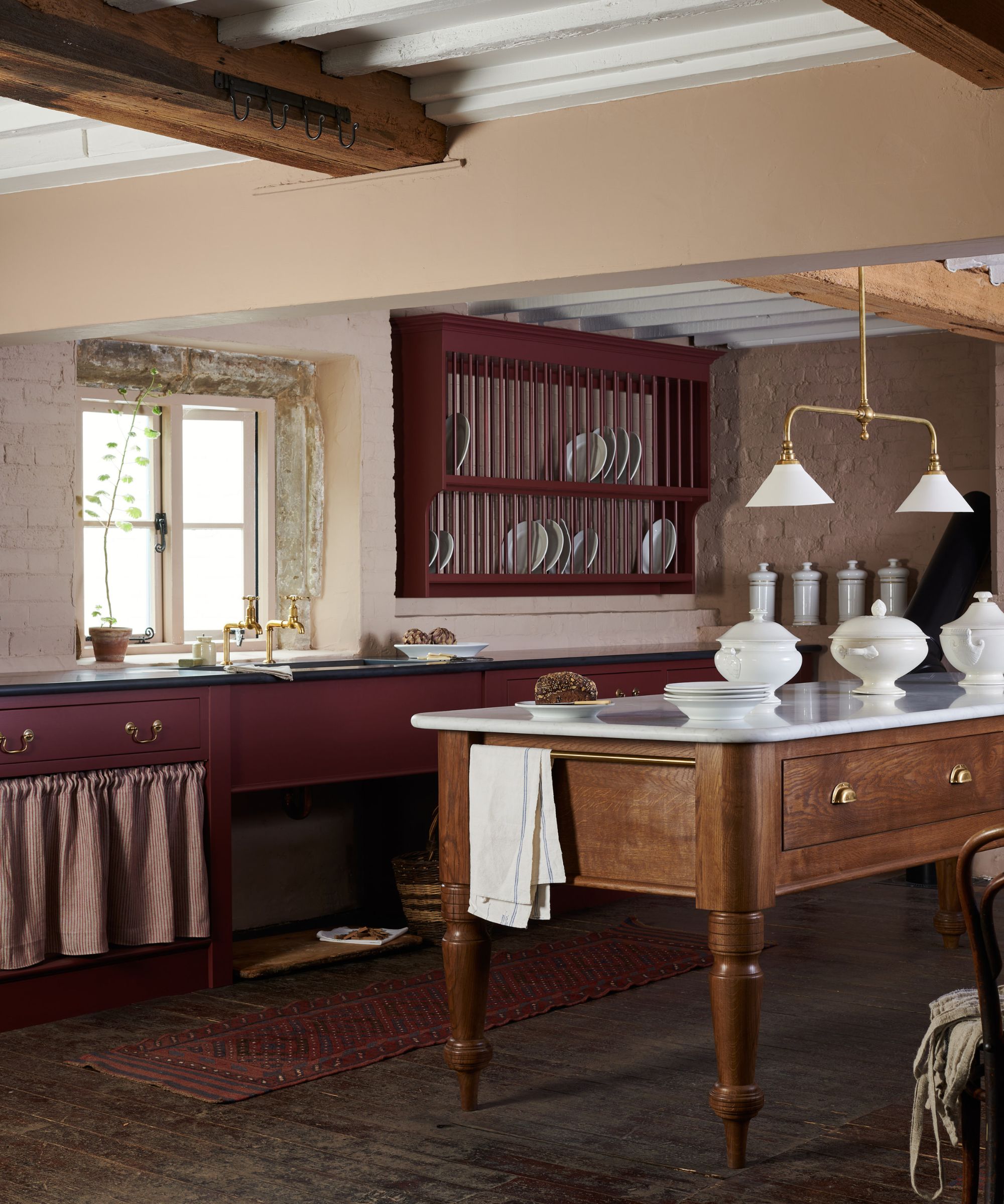 Traditional deVOL kitchen with a wall-mounted plate rack displaying white crockery, burgundy cabinetry and a freestanding Dairy Table with a marble worktop.