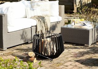 Dakota Fields Cattrall Steel Charcoal Fire Pit in a bricked garden with an outdoor sofa and coffee table