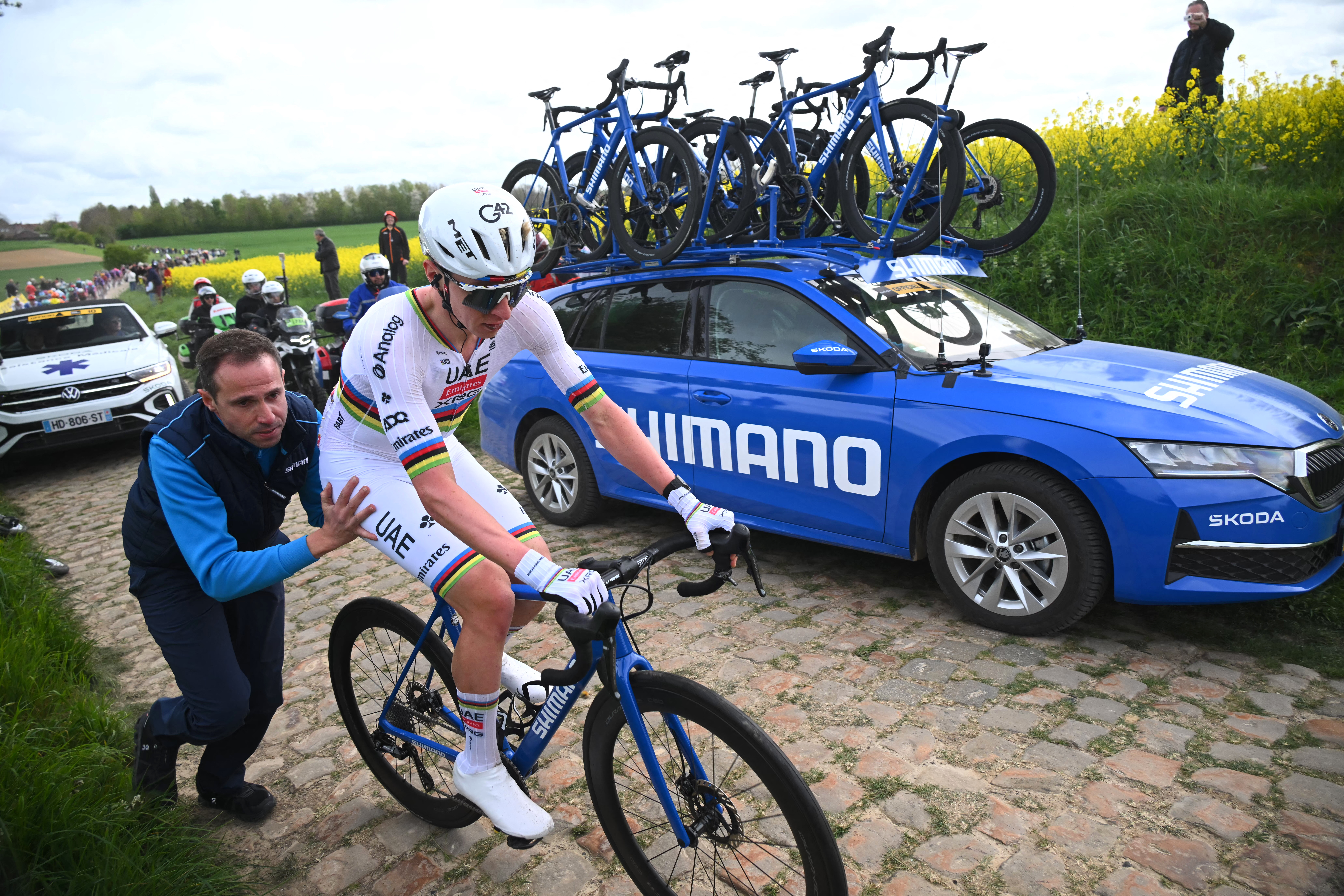 A side shot of a Shimano mechanic pushing Tadej Pogačar to get going again on a cobbled section at Paris-Roubaix, having swapped onto a neutral service bike after a mechanical