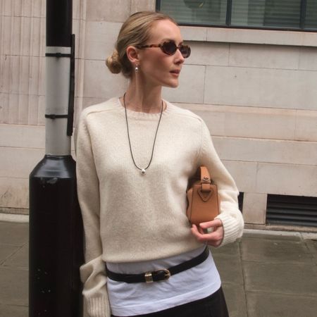 Woman wears cream jumper and carries beige bag