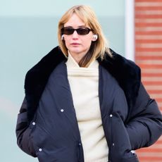 Jennifer Lawrence walks down the street in New York wearing a puffer jacket with a butter yellow jumper and a pink scarf tied around her waist.