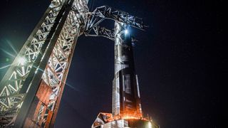 a silver spacex super heavy booster is lowered onto a launch platform at night