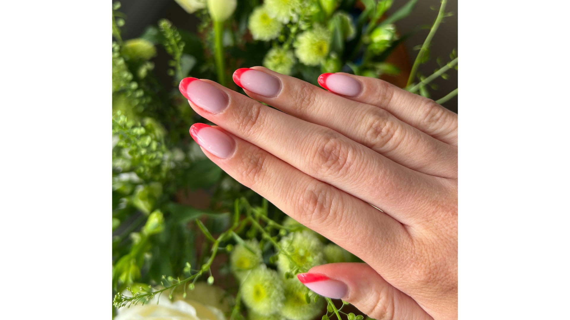 A close-up of Digital Beauty Writer, Sennen Prickett's coral French tip nails, in front of a leaf and flower background