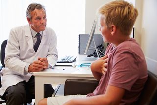 A doctor talks with a teen boy.