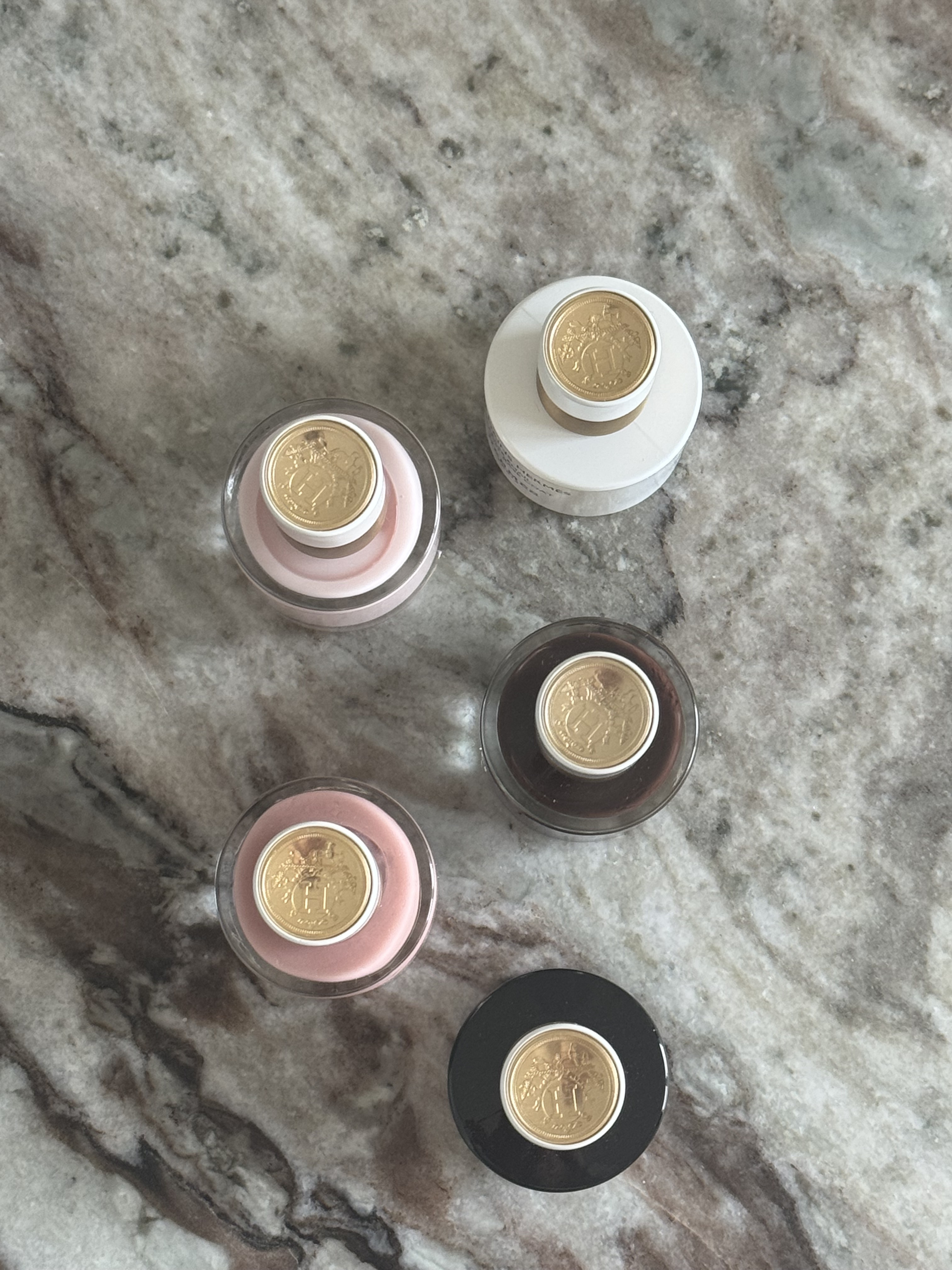 Hermes nail polish bottle tops with gold emblems, dotted around on a marble stone background