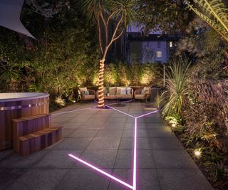 A patio garden with strip lighting built into the paving and LEDs wrapped around a tree trunk