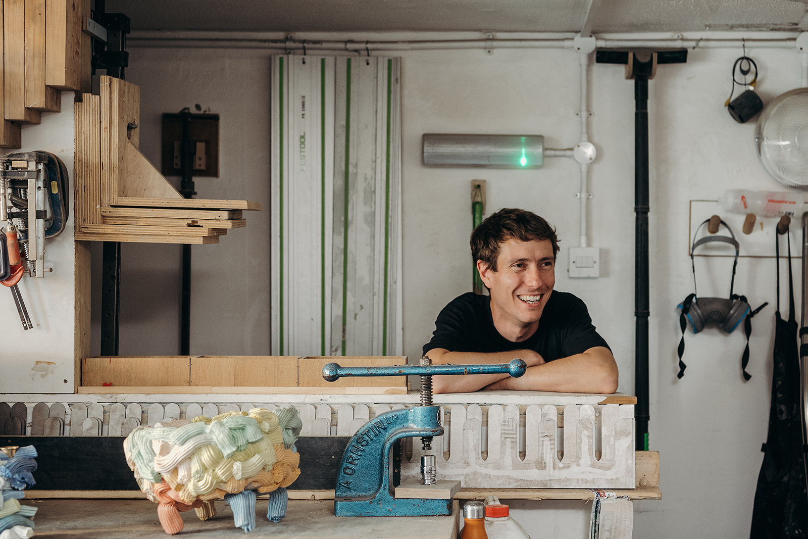 A young artisan caught smiling in his workshop while wearing a black T-shirt.