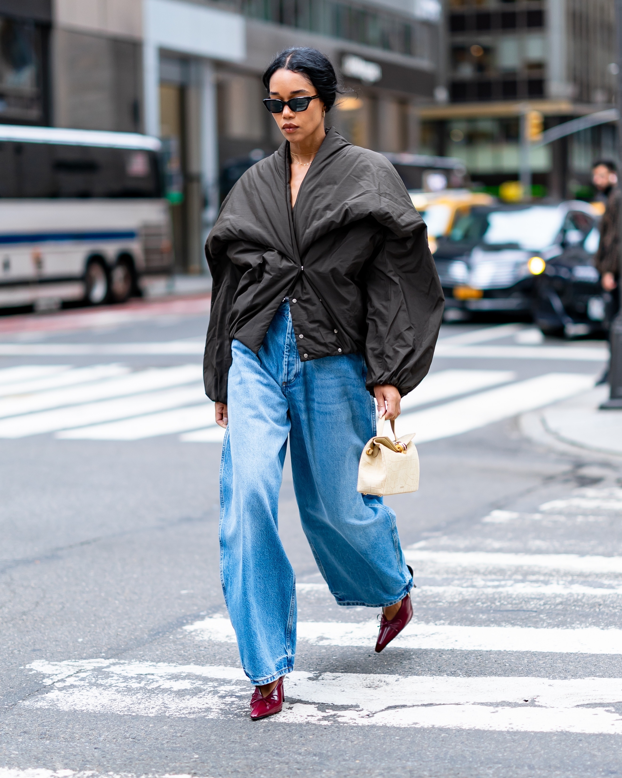 Laura Harrier walks down the street in New York wearing red heels with jeans and a puffer jacket.