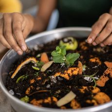 Hands touching soil and food waste in a bowl