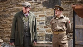 Duncan Preston in a flat cap as Enoch Sykes stands with Callum Woodhouse as Tristan in the All Creatures Great and Small Christmas Special 2024.